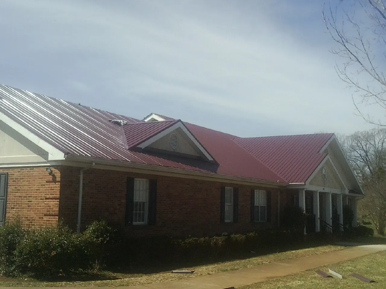 Red metal roof with gabled entries on a long brick building, from a Hail Damage Roof Repair job in Jamaica