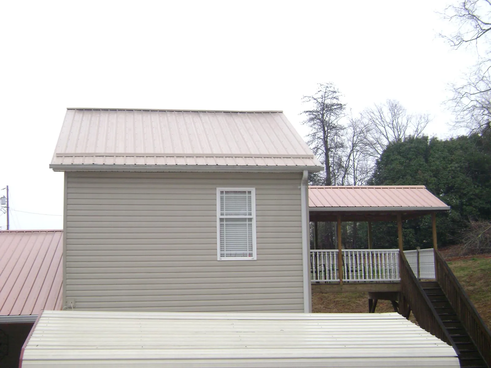 Tan metal roofs on a two story addition and attached porch, from a Roof Replacement job in Jamaica