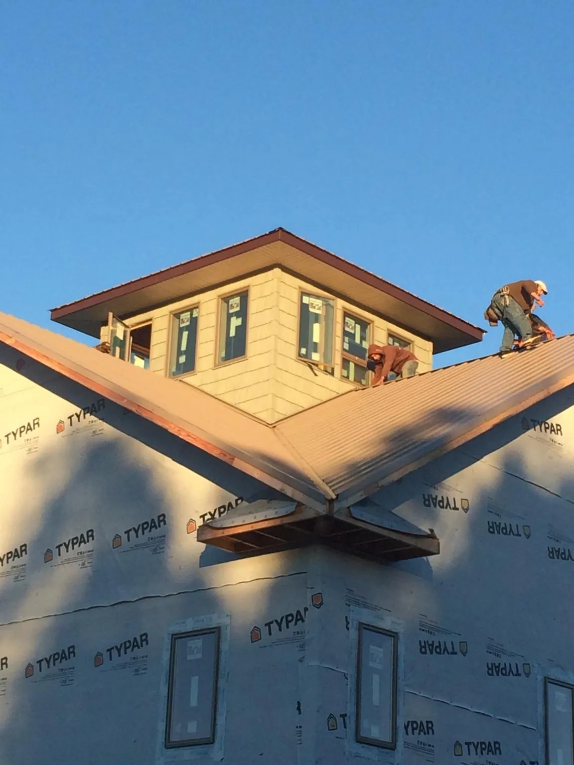 Roofers working around a rooftop cupola on a new metal roof at sunset — Roof Waterproofing in Jamaica by Roofing Brothers
